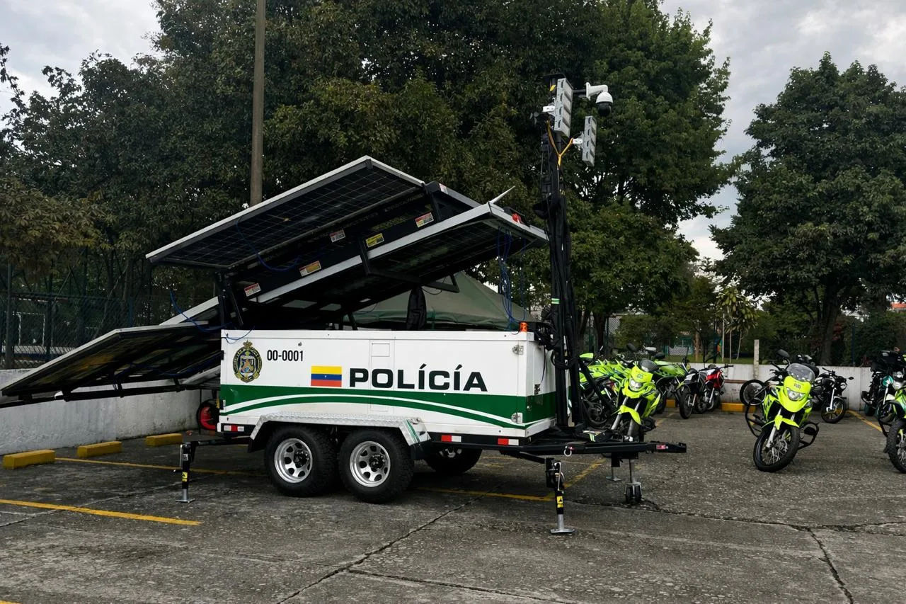 Remolque solar de la Policía con un mástil de cámaras y reflectores, estacionado junto a motocicletas policiales.