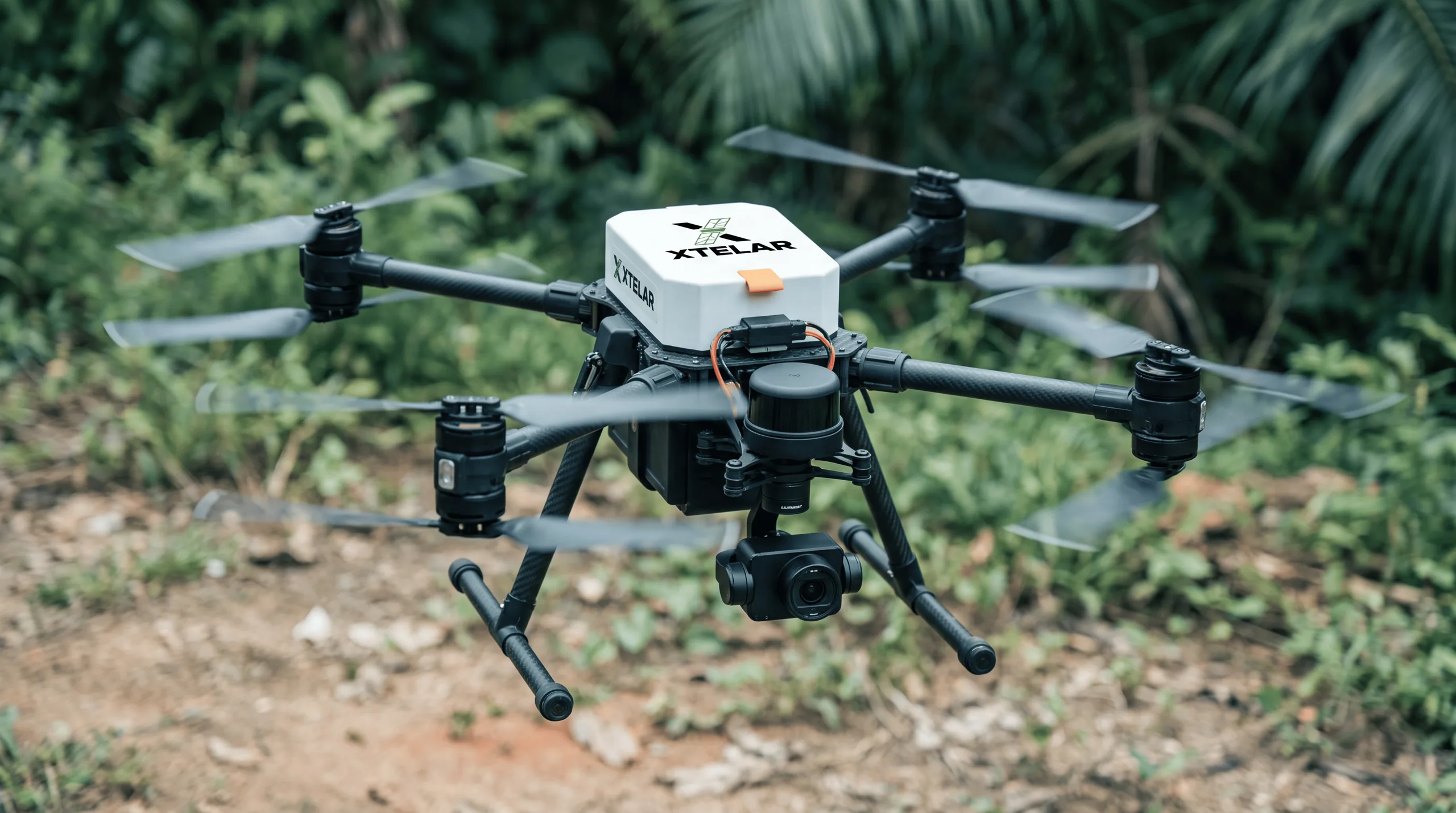Dron cuadricóptero negro con la marca Xtelar y una cámara estabilizada, en vuelo bajo frente a vegetación tropical.
